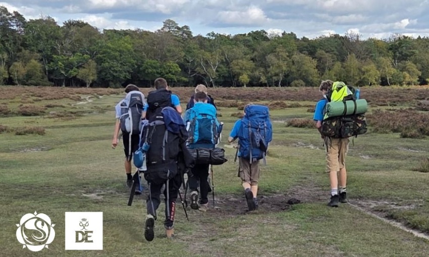 A group of students wearing large rucksacks hiking along a path through countryside terrain during a Duke of Edinburgh's Award expedition